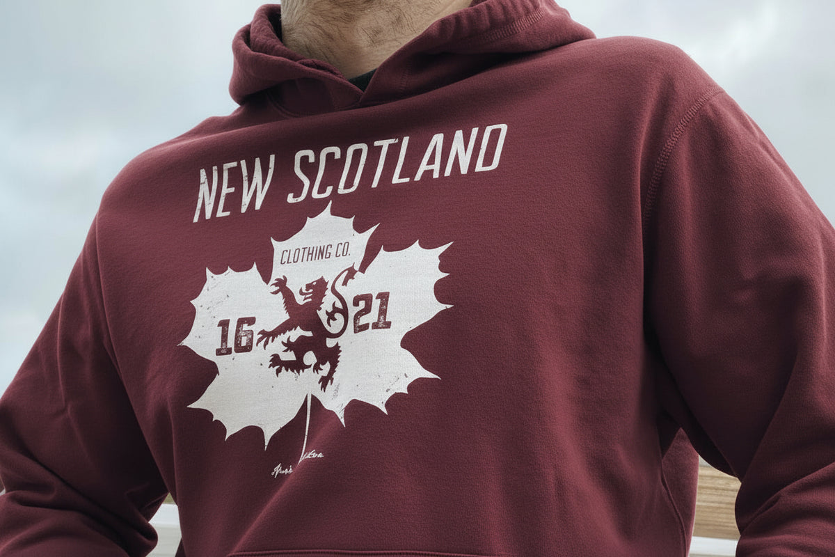 Red hoodie with 'New Scotland' and lion emblem design on a person sitting outdoors.